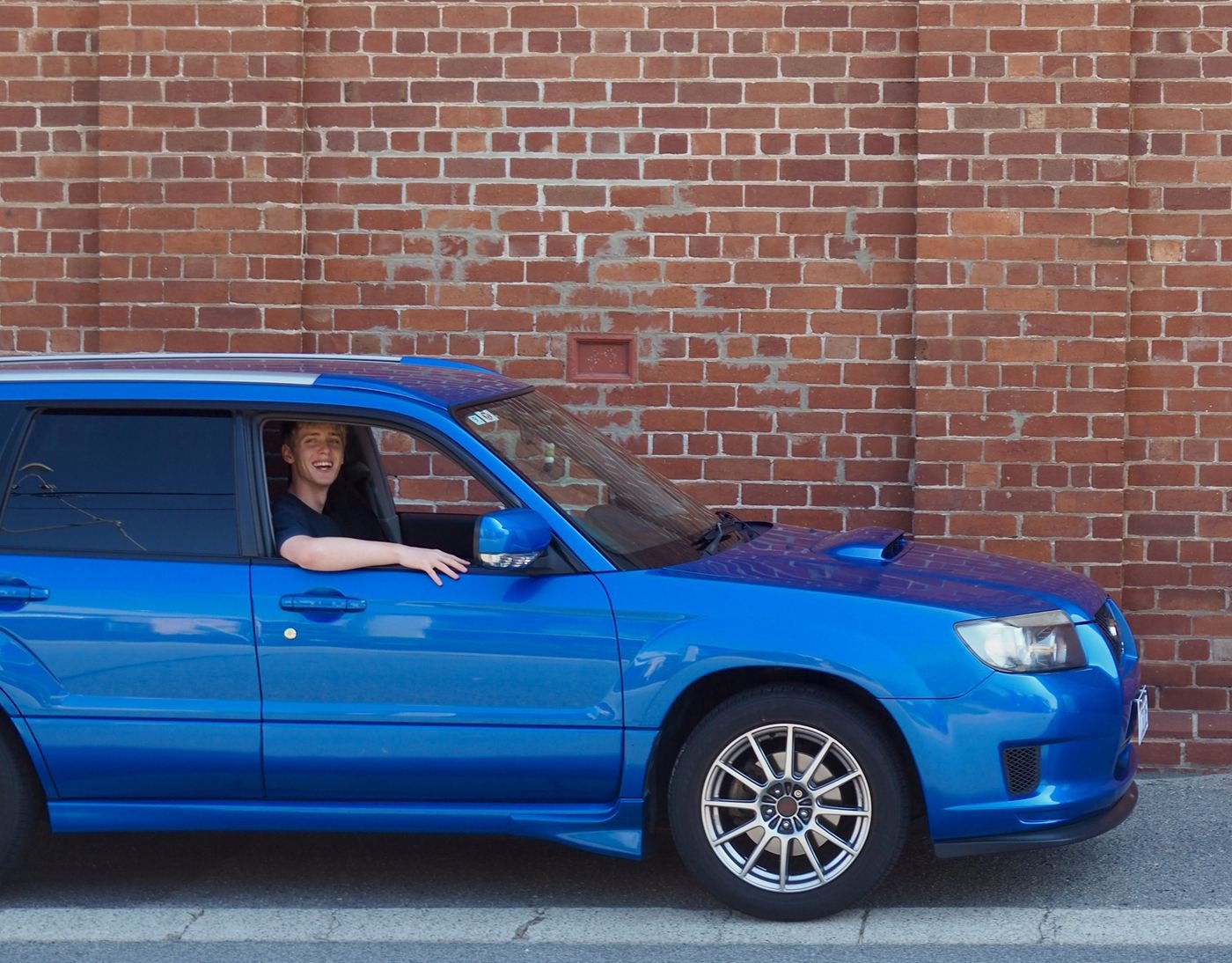 Rory in the driver's seat of his blue 2006 Subaru Forester, arm resting out the window