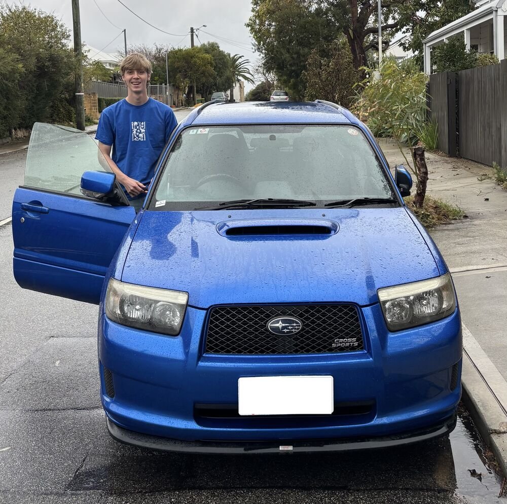 Rory standing beside his blue 2006 Subaru Forester